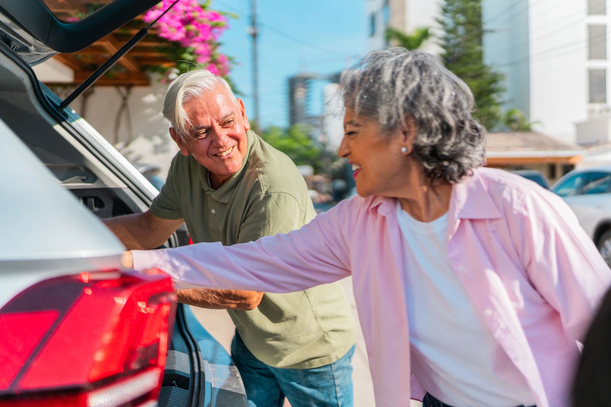 Senior couple with luggage walking toward a car trunk outdoors